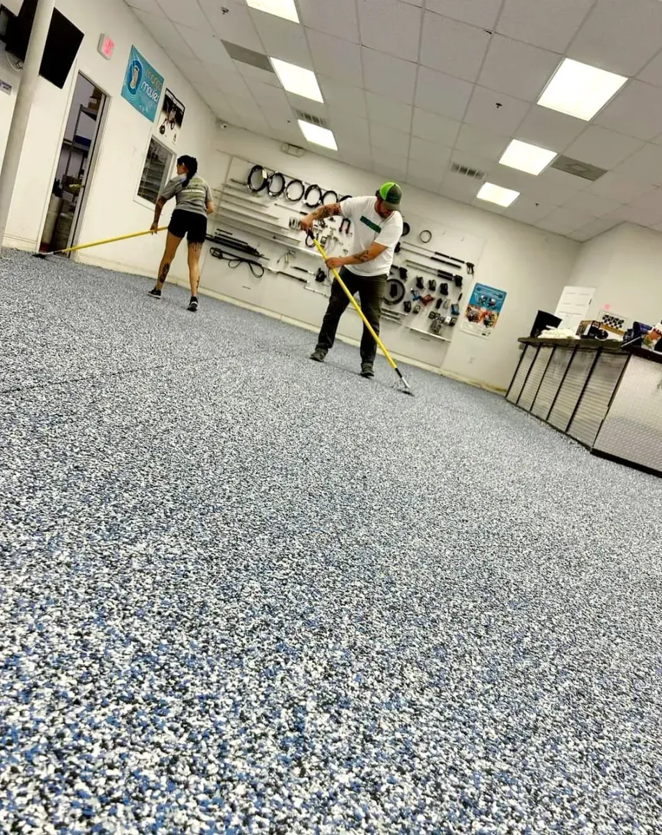 Two people practicing in a bright dance studio with a speckled floor and mirrors on the wall.