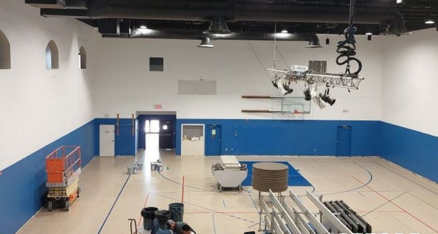 Empty gymnasium with blue lower walls, white upper walls, and equipment carts under a high ceiling.