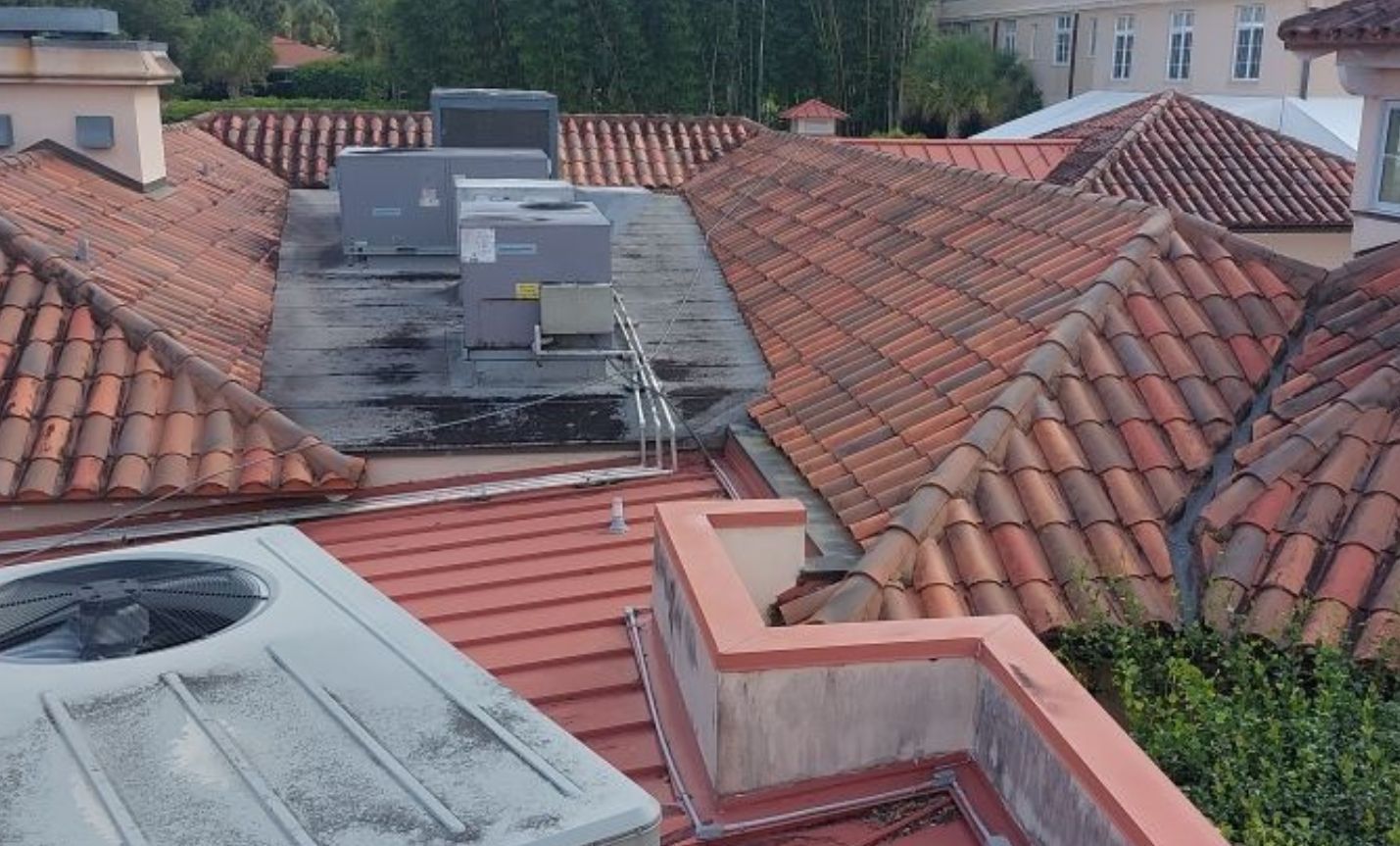 Rooftop view of red clay tiles and gray HVAC units on a building in a dense urban area