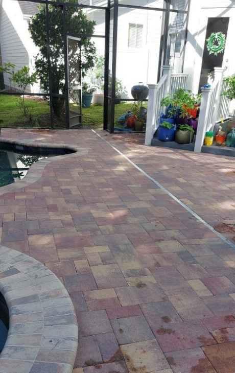 Brick patio by a pool with white posts and colorful flower pots in a greenhouse-like courtyard