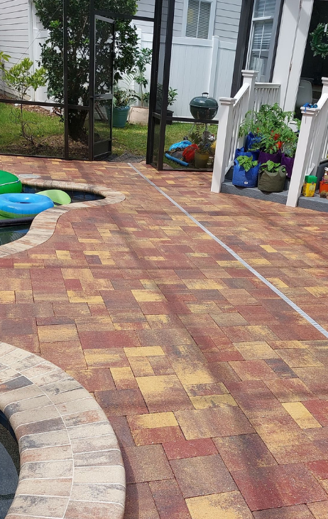 Backyard patio with red and yellow brick pavers, potted flowers, and a gate by a house