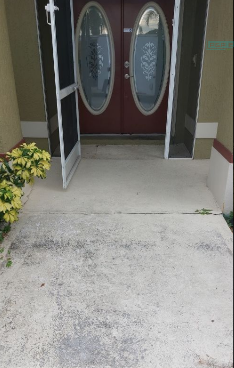 Front entrance with open doors, concrete walkway, and potted flowers on the left side.