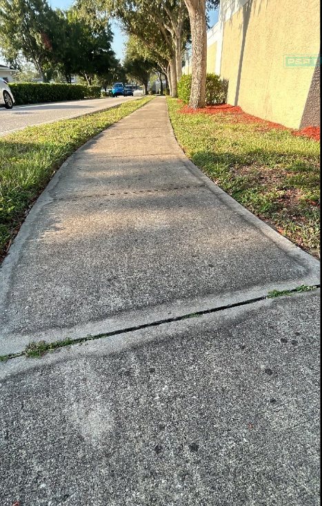 Concrete sidewalk beside a grassy verge and yellow wall in a sunny residential area