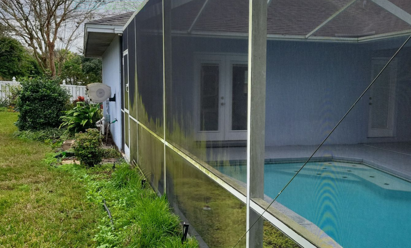 Screened-in patio beside a blue house, with a swimming pool visible behind the mesh.