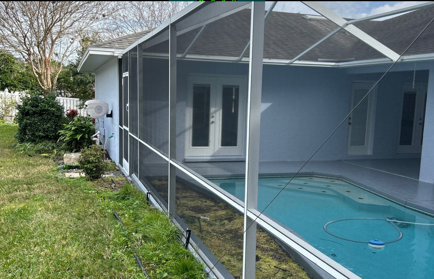 Screened pool enclosure beside a house with a blue pool and grassy yard