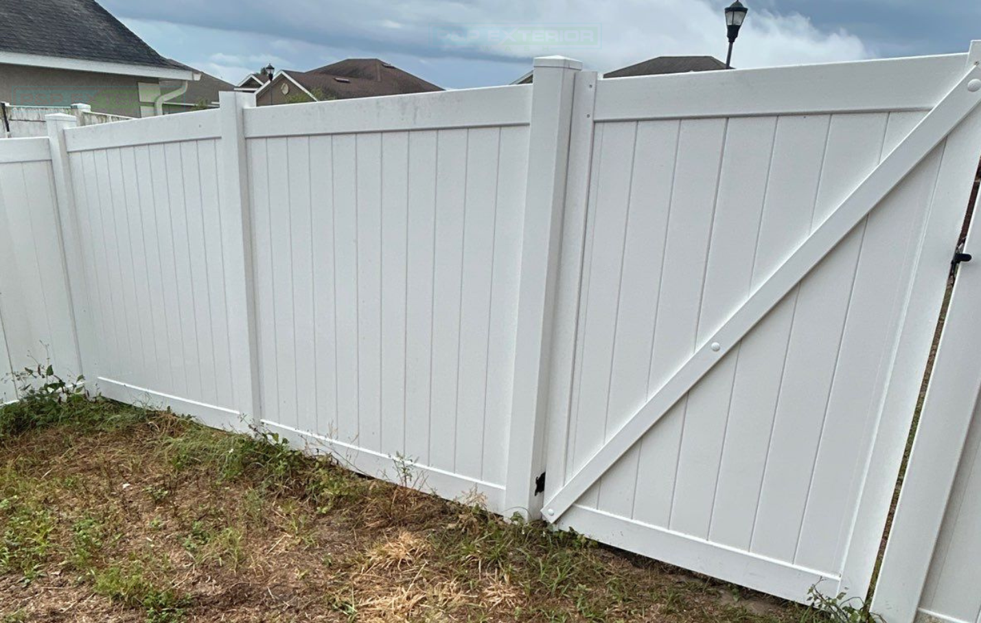 White vinyl fence with diagonal support brace and gate in a grassy backyard under a cloudy sky