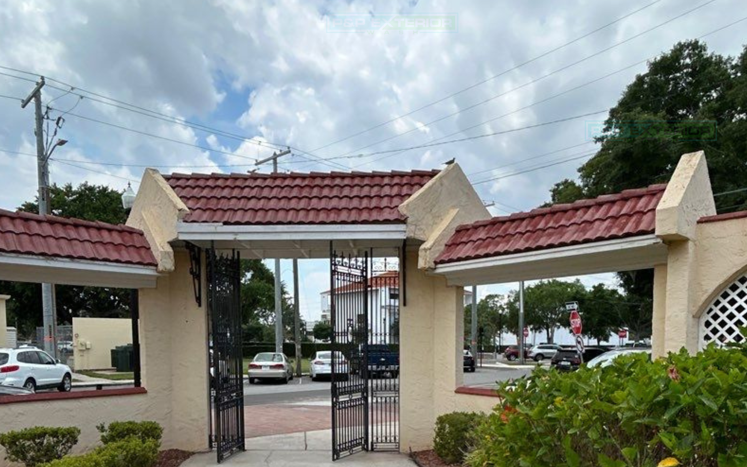 Entrance gate with red tiled roof, beige pillars, and open black metal gates in a street setting