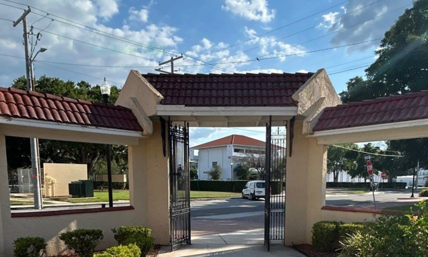 Entrance gate to a building complex with red-tiled roofs and a parked car beyond