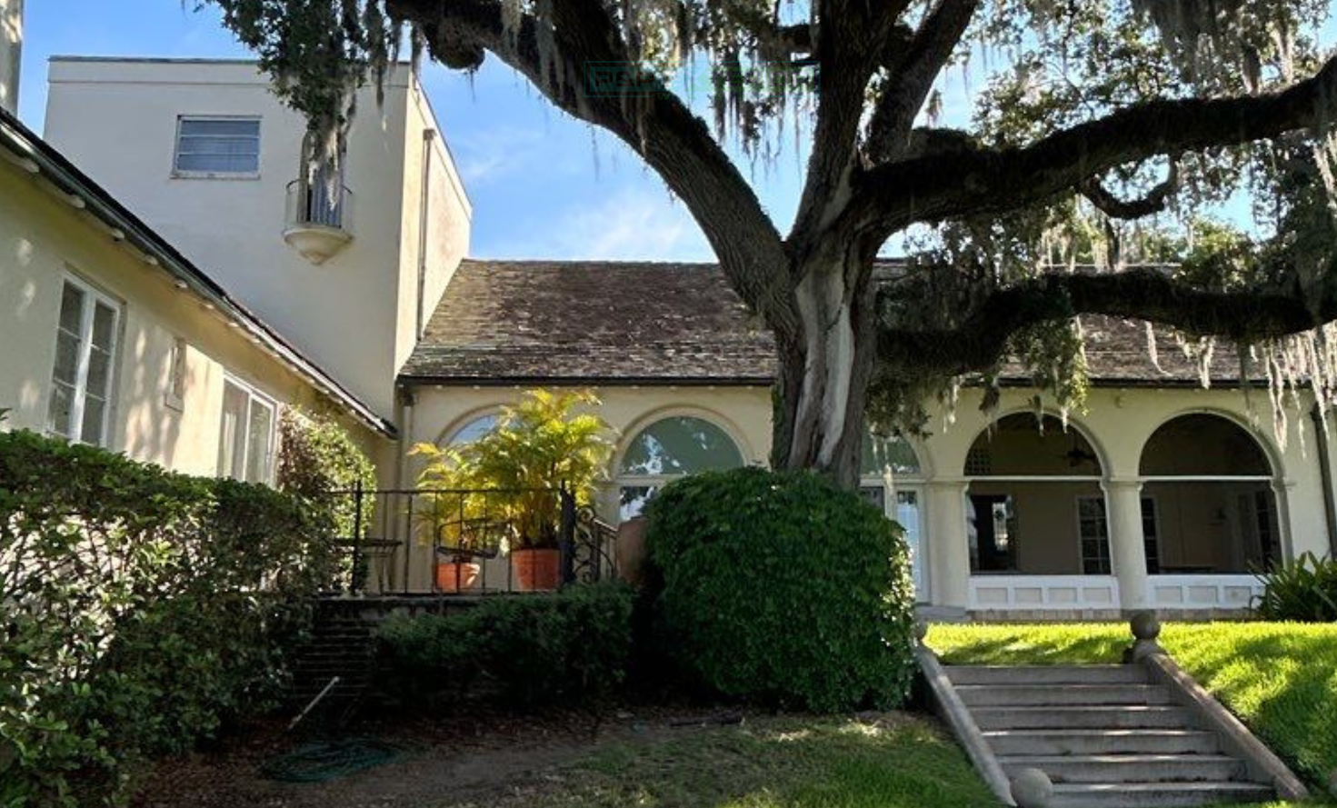 Spanish-style building with arched windows, large oak tree, and sunlit courtyard steps