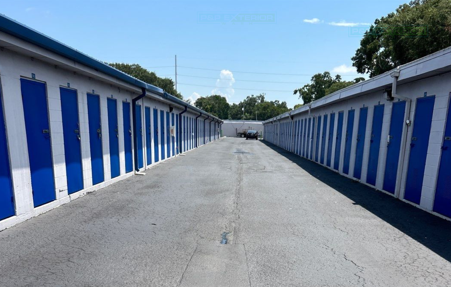 Rows of blue-and-white storage units line a paved driveway under a clear sky.