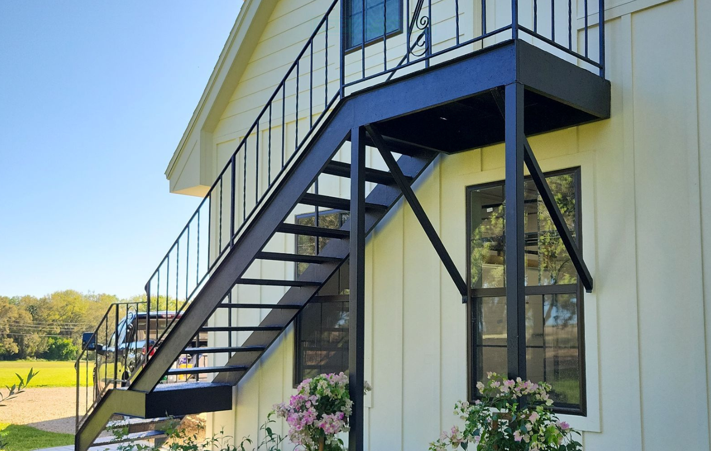 Exterior metal staircase attached to a white building with large windows and a balcony.