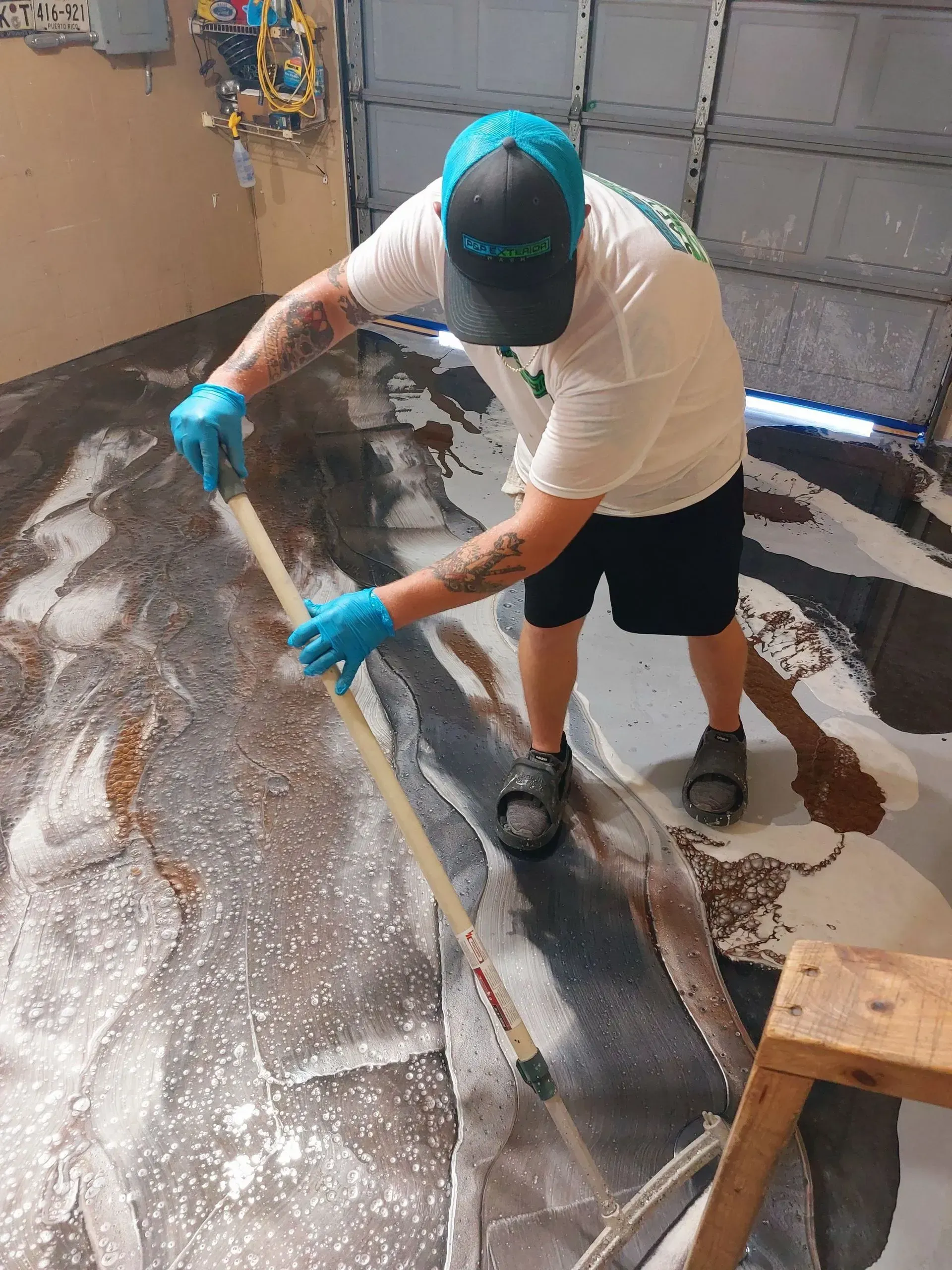 Person cleaning a floor with a squeegee, wearing blue gloves and a cap in a wet indoor space