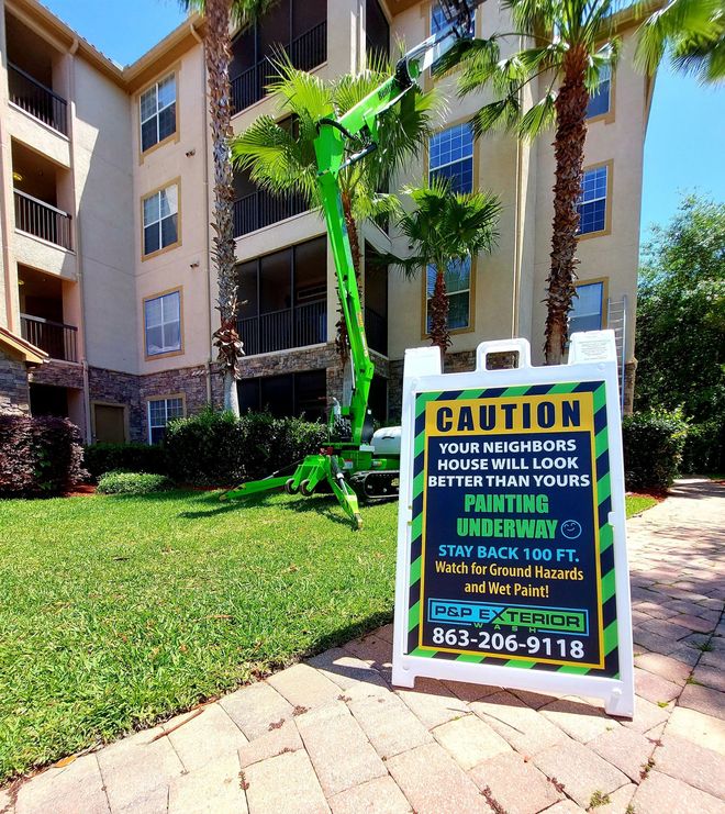 Apartment courtyard with a yellow caution sign on the sidewalk near green lawn and palm trees