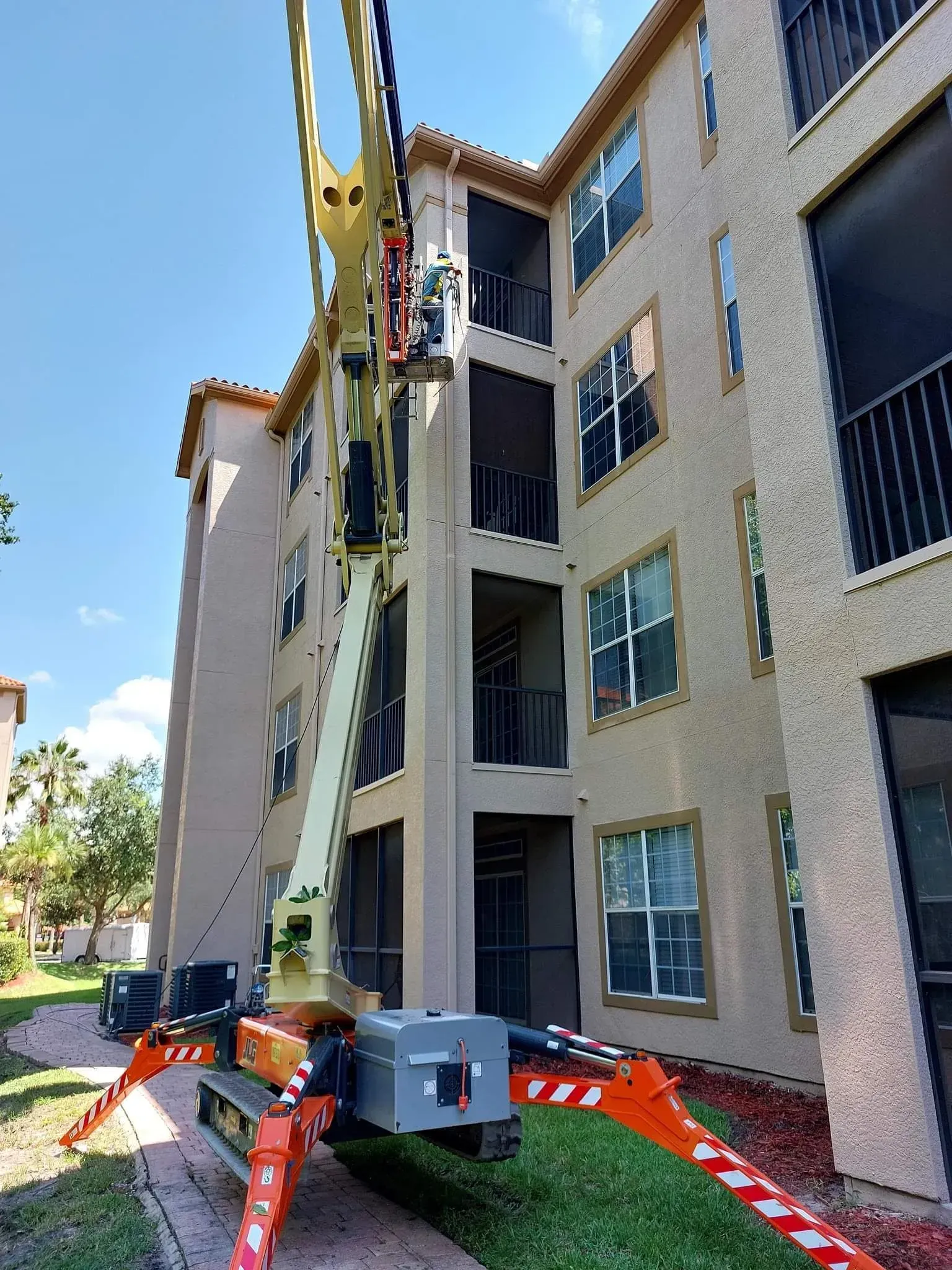 Construction lift beside an apartment building, with orange safety barriers and parked cars nearby.
