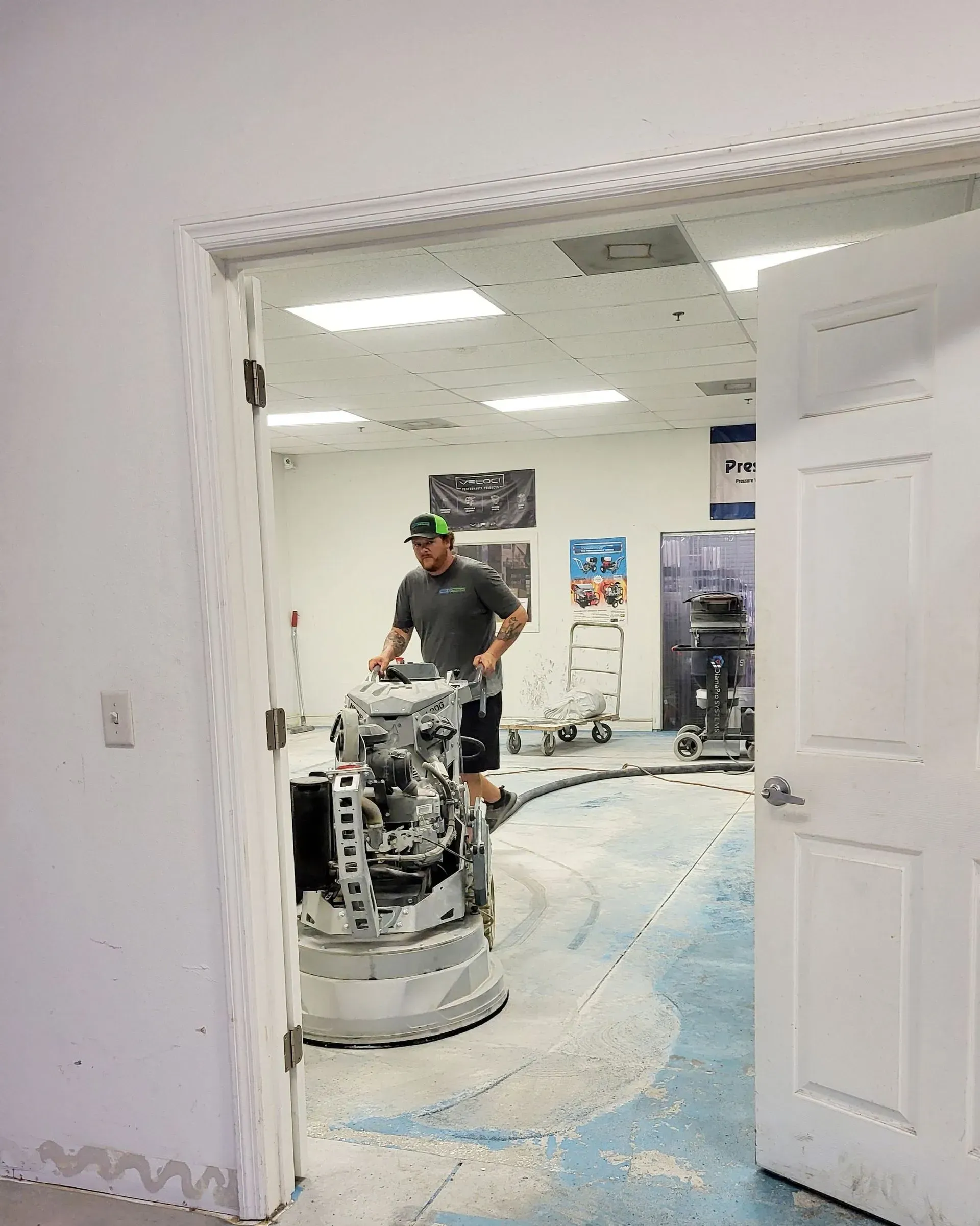 Person with a floor buffer in a carpeted room, seen through an open doorway.