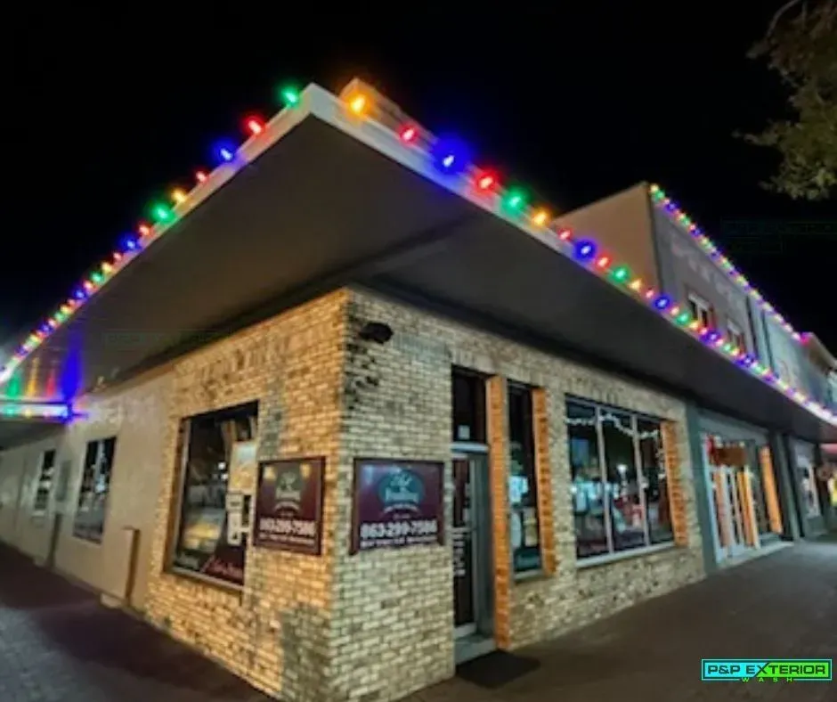 Brick corner building at night, outlined with colorful Christmas lights and lit storefront windows.