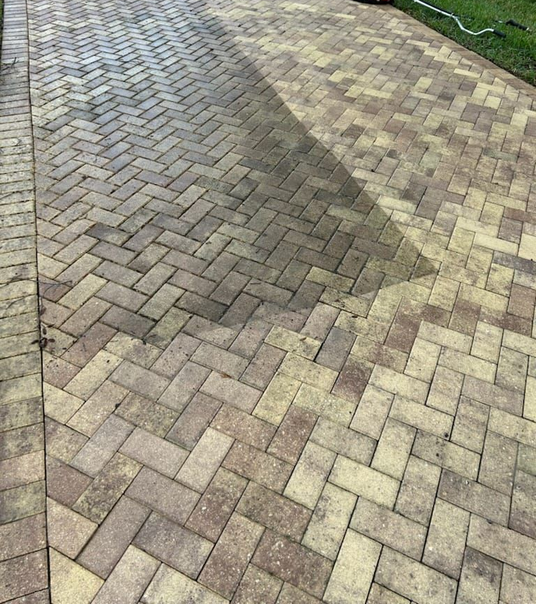 Brick-paved driveway with a darker repaired patch and lighter surrounding pavers.