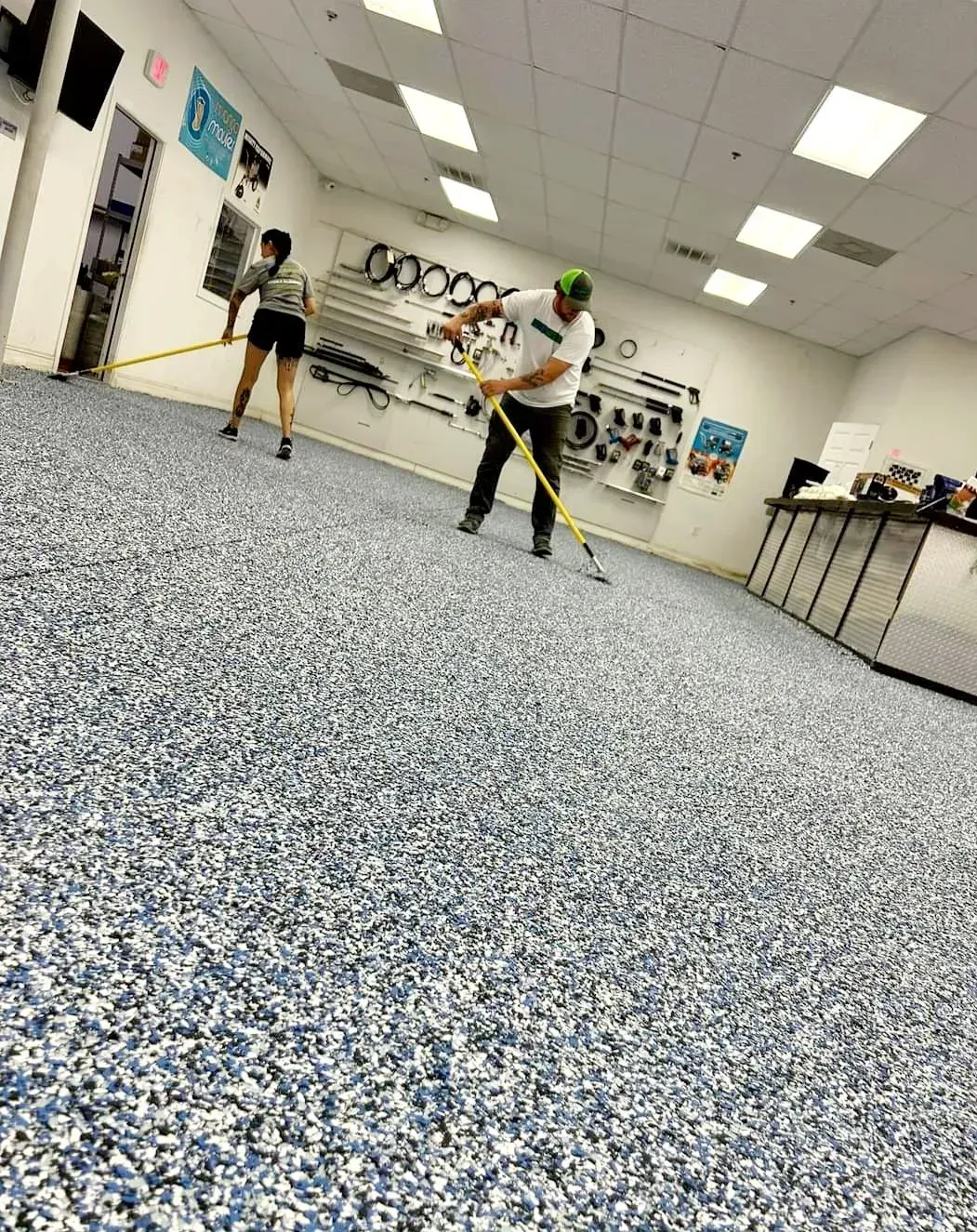 Two people playing floor hockey in a bright indoor room with speckled flooring.