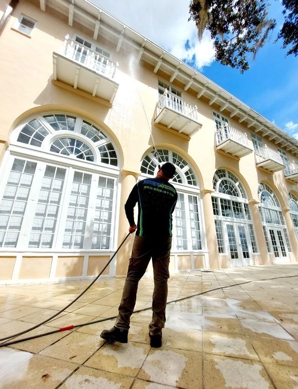 Person power-washing a cream-colored building with arched windows and balconies on a sunny day