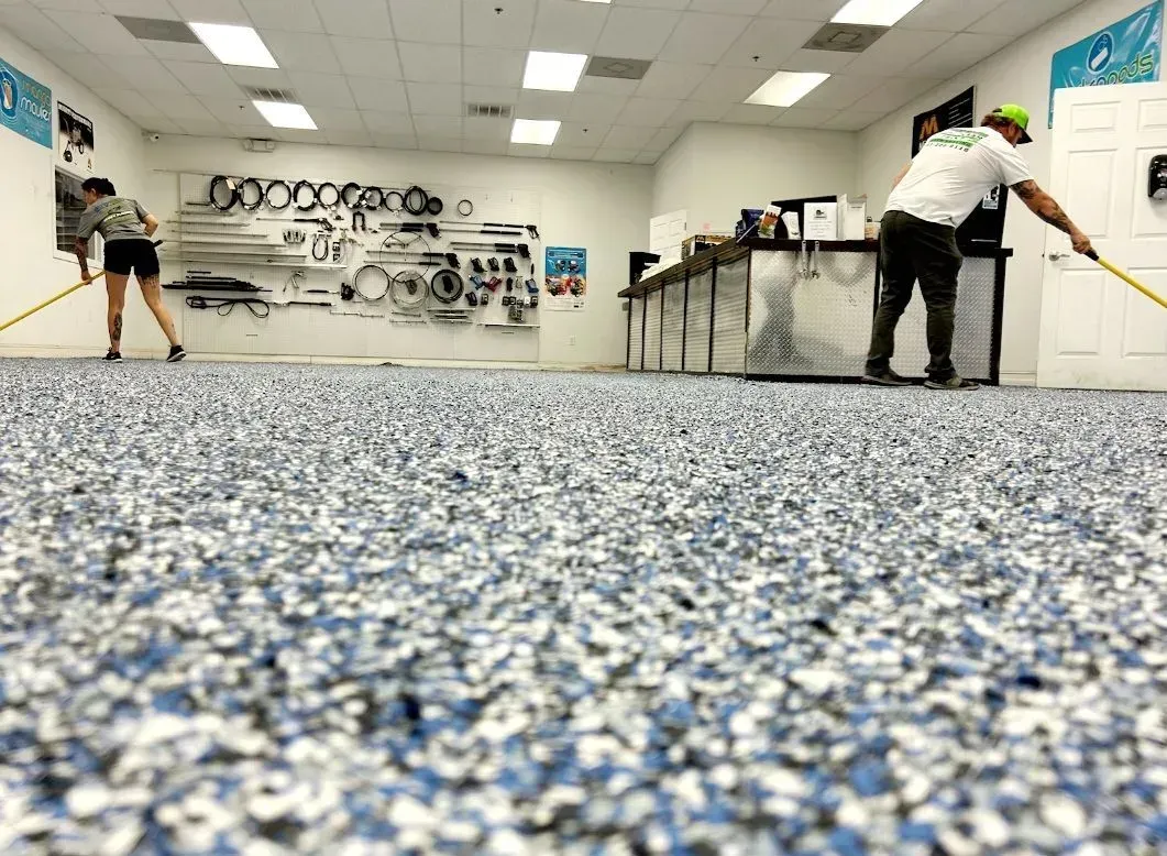 People working in a bright room with a speckled blue floor, painting or cleaning walls and tables.