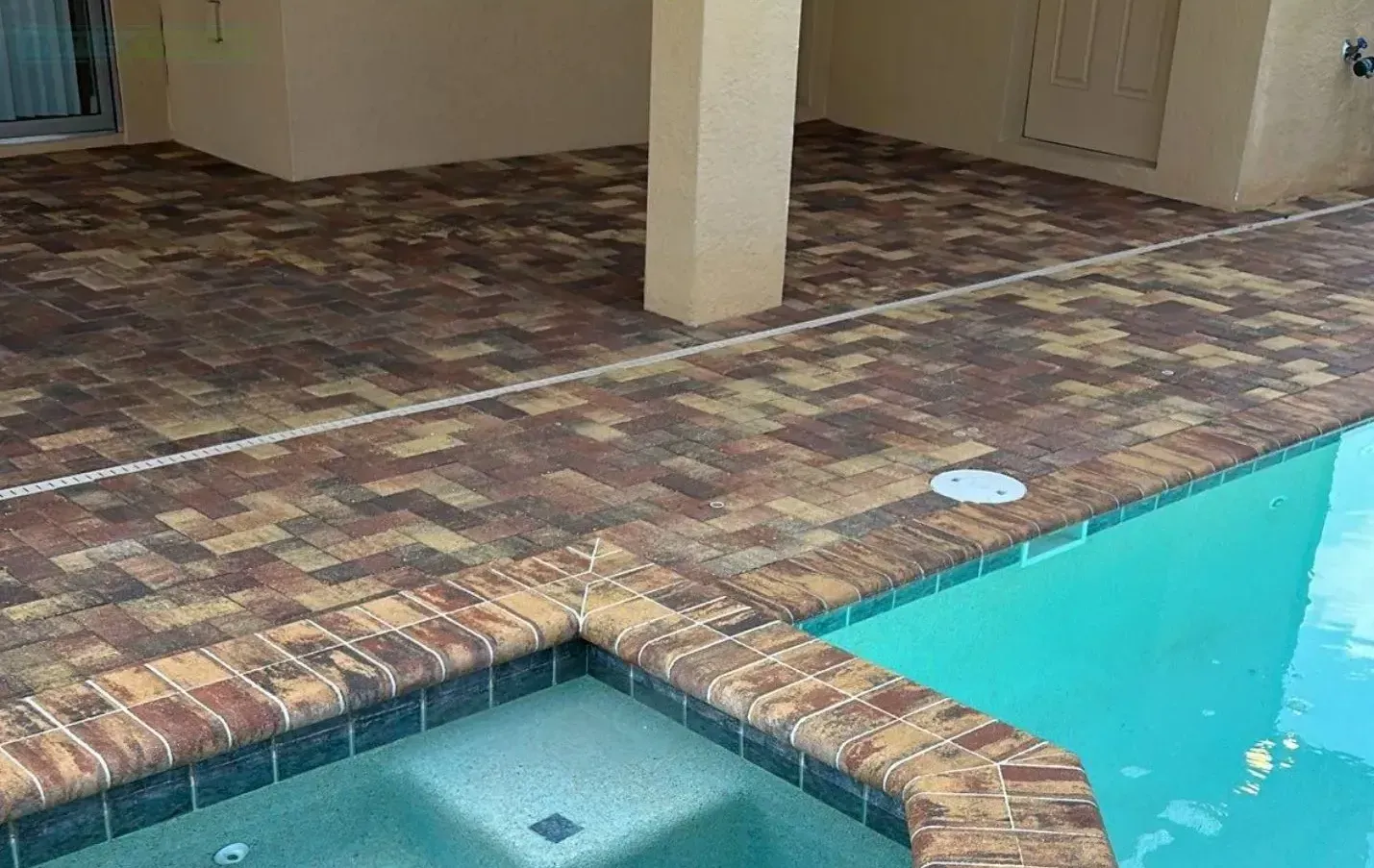 Covered patio beside turquoise swimming pool with brick pavers and columns