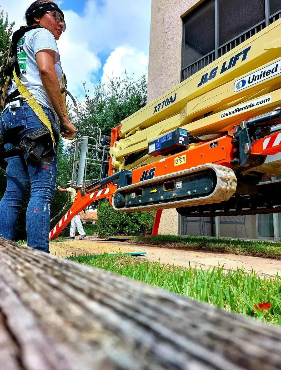 Worker beside a yellow/orange construction lift on a sidewalk near a building