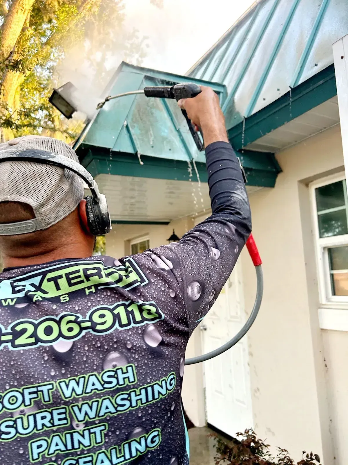 Worker power-washing a turquoise awning beside a house exterior.