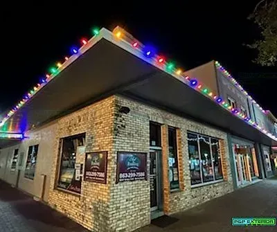 Brick corner building at night, outlined with colorful holiday lights and lit storefront windows.