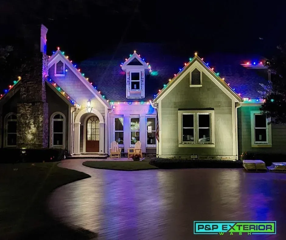 House exterior lit with colorful holiday lights at night, with a paved driveway in front.