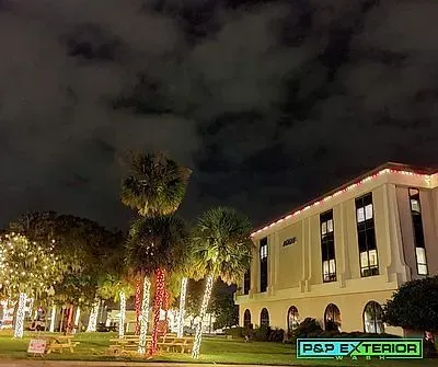 Nighttime exterior of a lit building with palm trees and cloudy sky, decorated with red and white lights.
