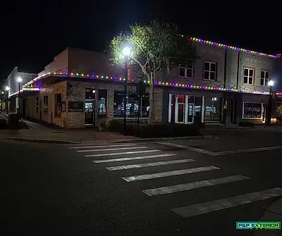 Nighttime street corner with a lit storefront, Christmas lights, and a crosswalk in front