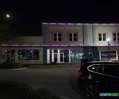 Nighttime street view of a storefront with colorful holiday lights and a parked car in front.