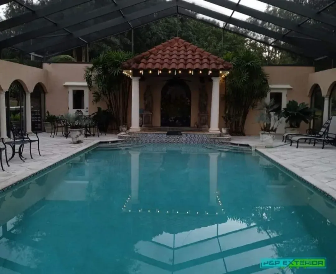Indoor swimming pool with turquoise water, white lounge chairs, and a tiled gazebo under a glass roof.