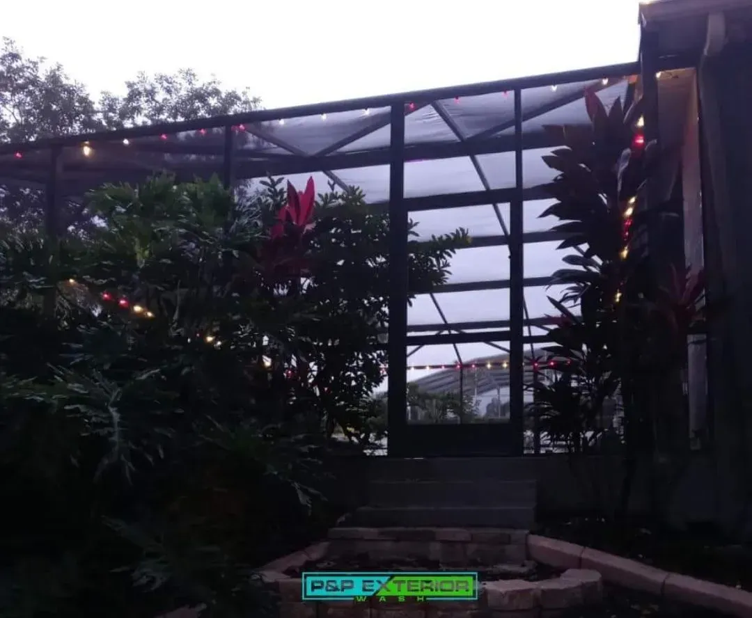 Garden pergola with lush plants, dark metal frame, and steps leading up to a walkway at dusk.