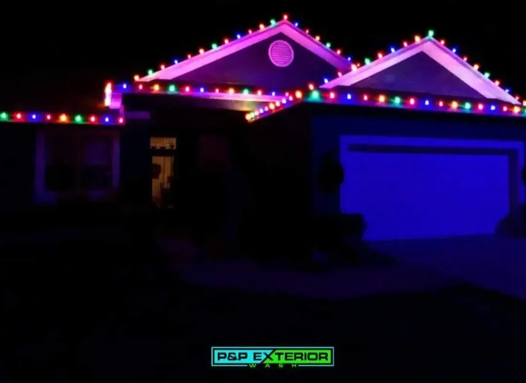House at night outlined with multicolored Christmas lights and a blue-lit garage.