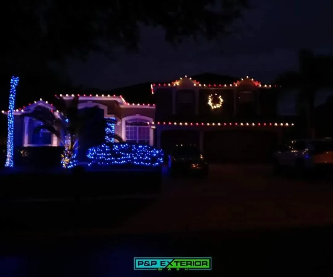 House at night decorated with blue, pink, and red Christmas lights and a glowing wreath