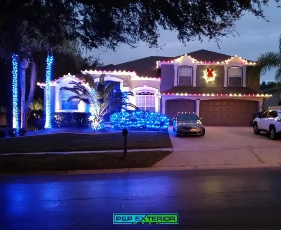 House decorated with blue and white holiday lights at dusk, with cars in the driveway.