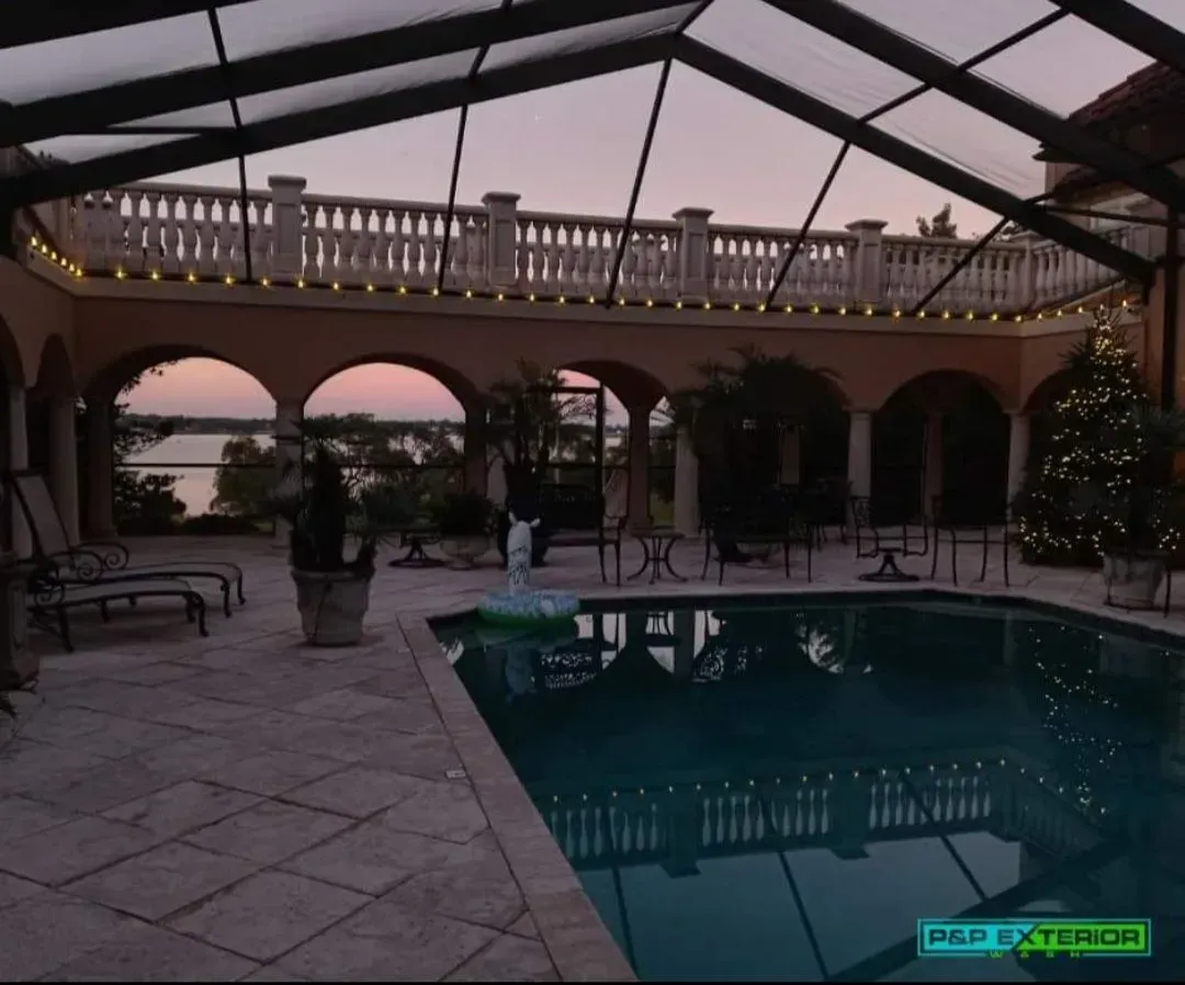 Covered pool patio with arches, tiled deck, benches, and string lights at dusk.