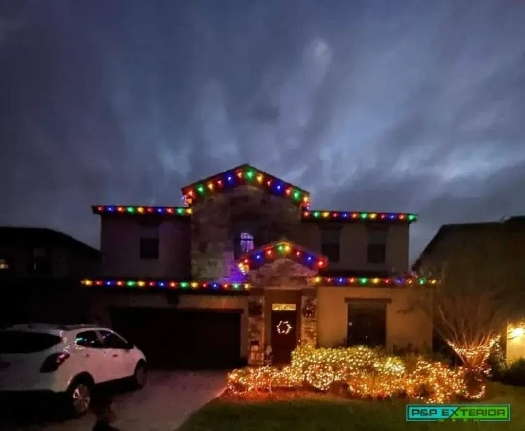 House decorated with colorful Christmas lights at dusk, with a white car in the driveway.