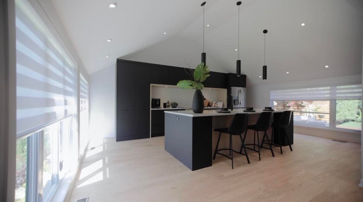 Cuisine moderne avec îlot noir, tabourets et suspensions, parquet en bois clair et mur foncé.