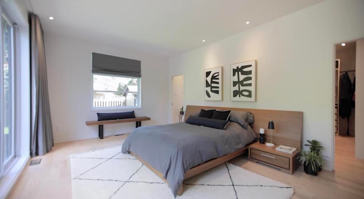 Chambre moderne avec literie grise, cadre de lit en bois, œuvres d'art et tapis.