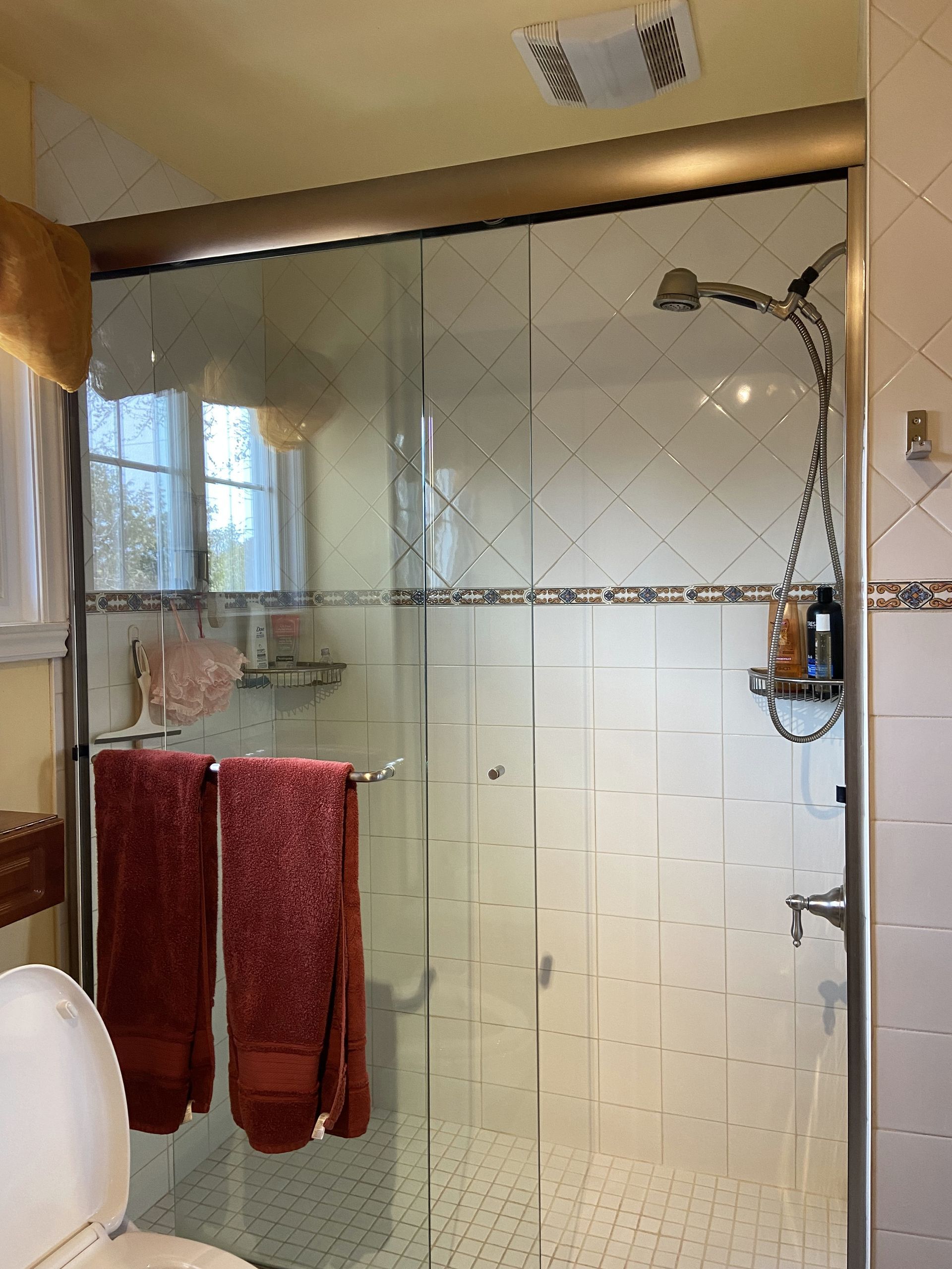 Une salle de bain avec une douche en verre, des serviettes rouges et des murs carrelés blancs.
