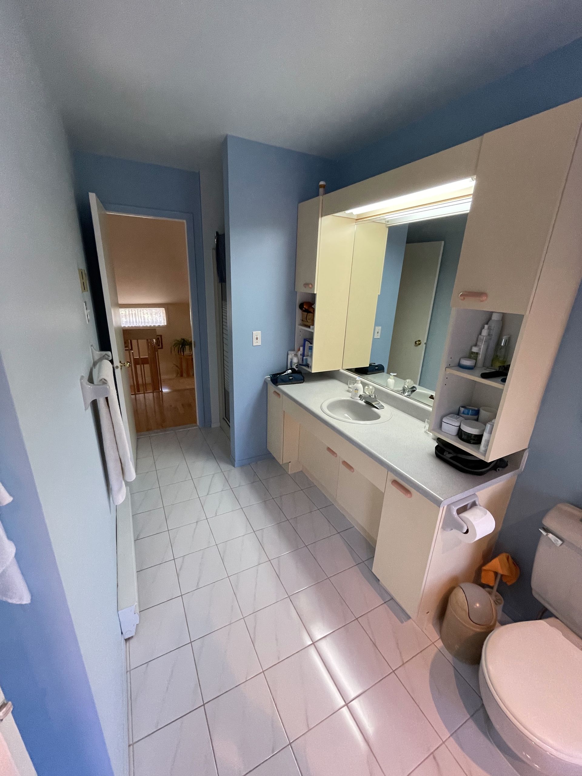 Salle de bain avec murs bleu clair, vanité blanche et sol en carrelage blanc ; une toilette est au premier plan.