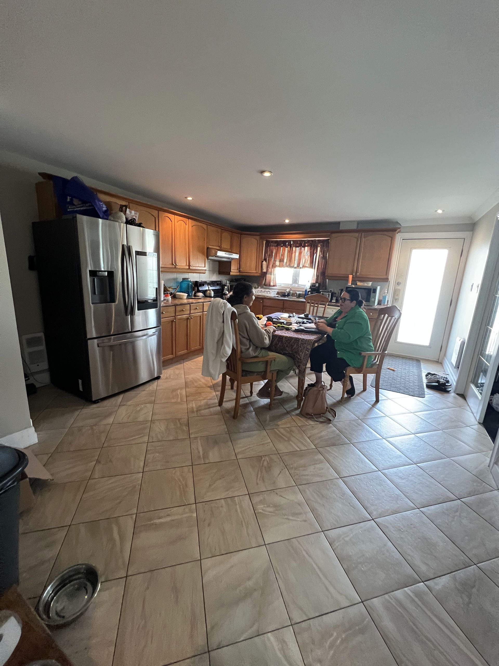 Deux femmes assises à une table dans une cuisine avec des appareils en acier inoxydable et des armoires en bois.
