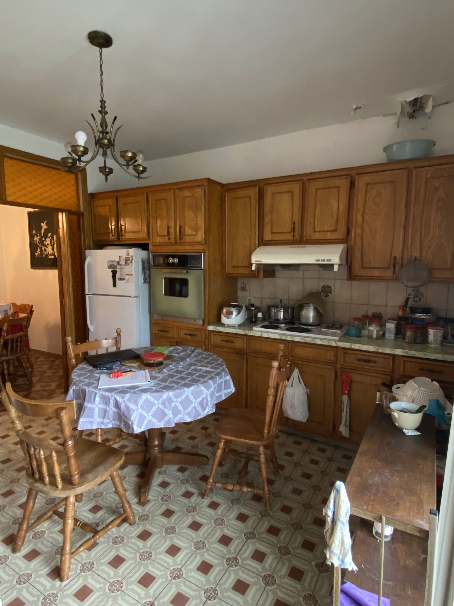 Cuisine avec armoires en bois, table ronde avec chaises et réfrigérateur.