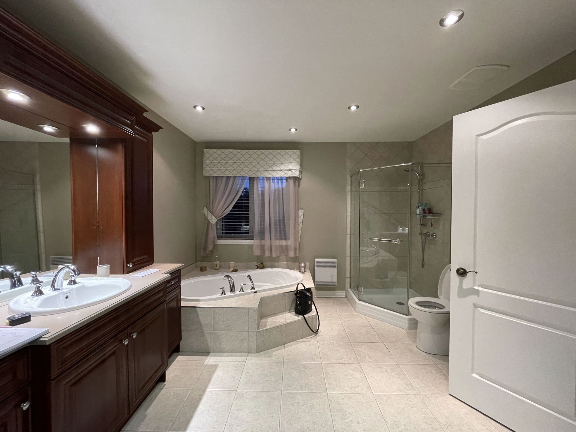 Salle de bain spacieuse avec une vanité en bois foncé, une baignoire jacuzzi, une douche et une porte blanche fermée.