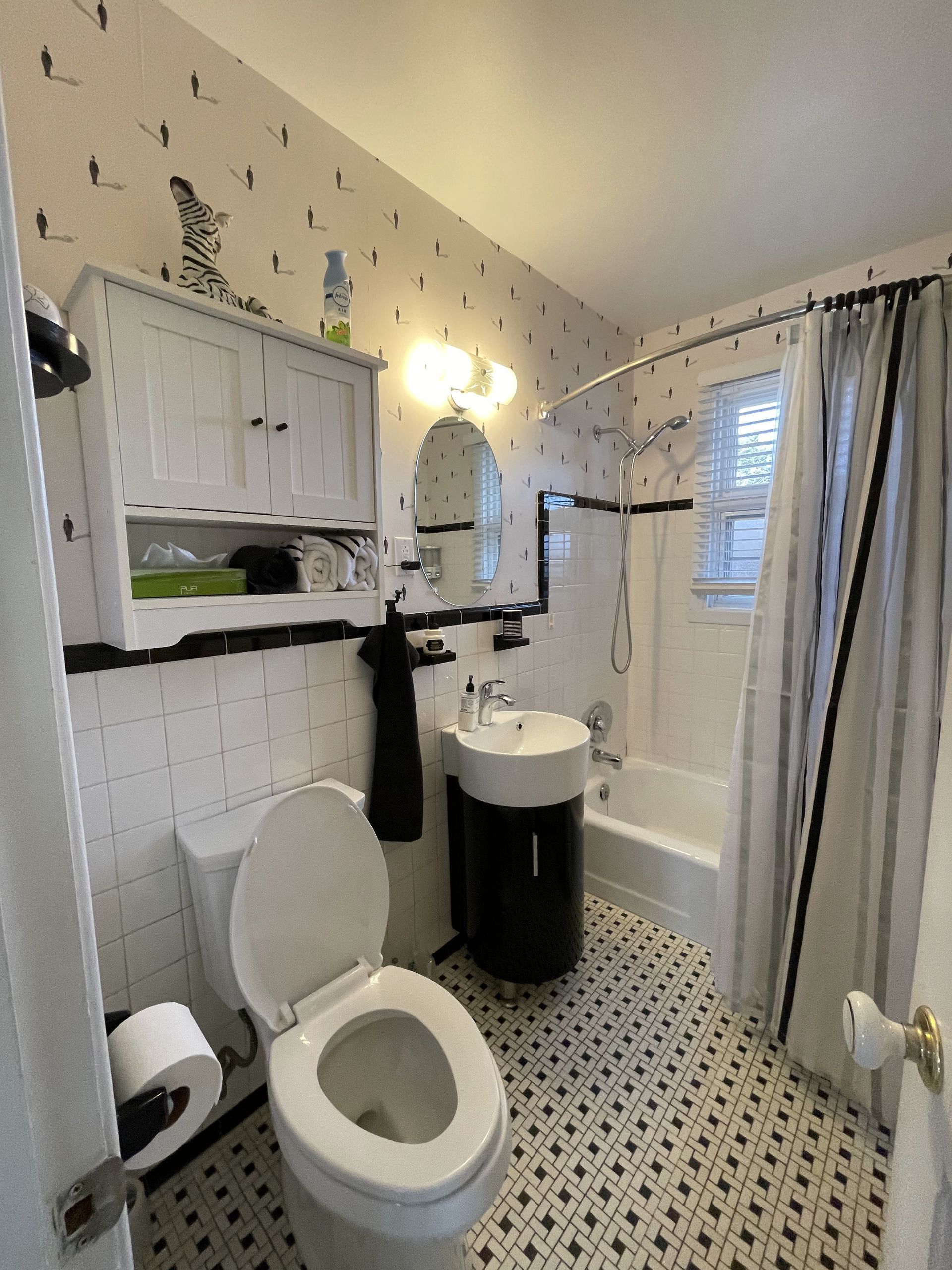 Salle de bain avec papier peint zèbre, carrelage noir et blanc et vanité noire.