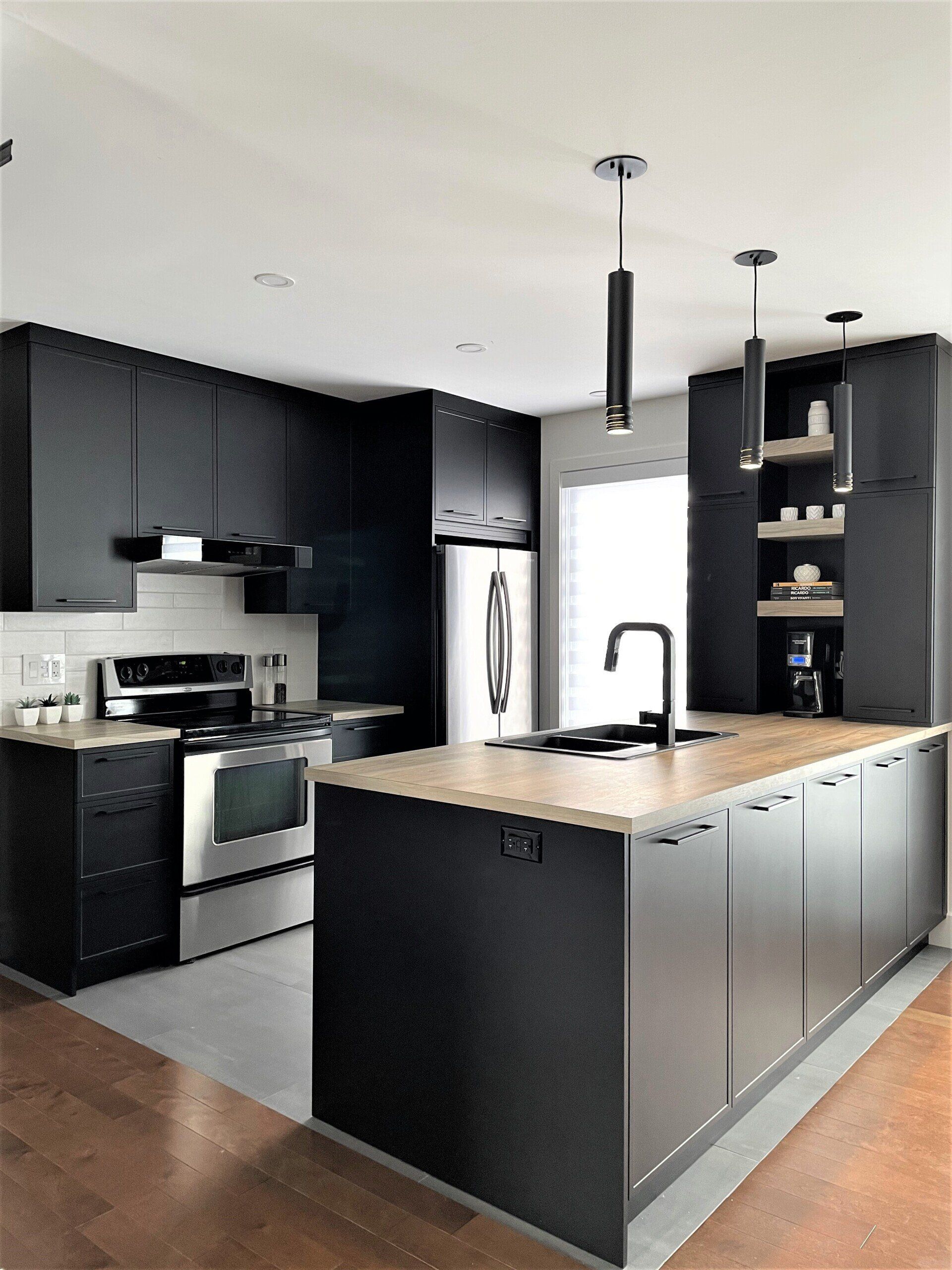 Cuisine moderne avec armoires noires, appareils électroménagers en acier inoxydable, comptoirs en bois clair et îlot.