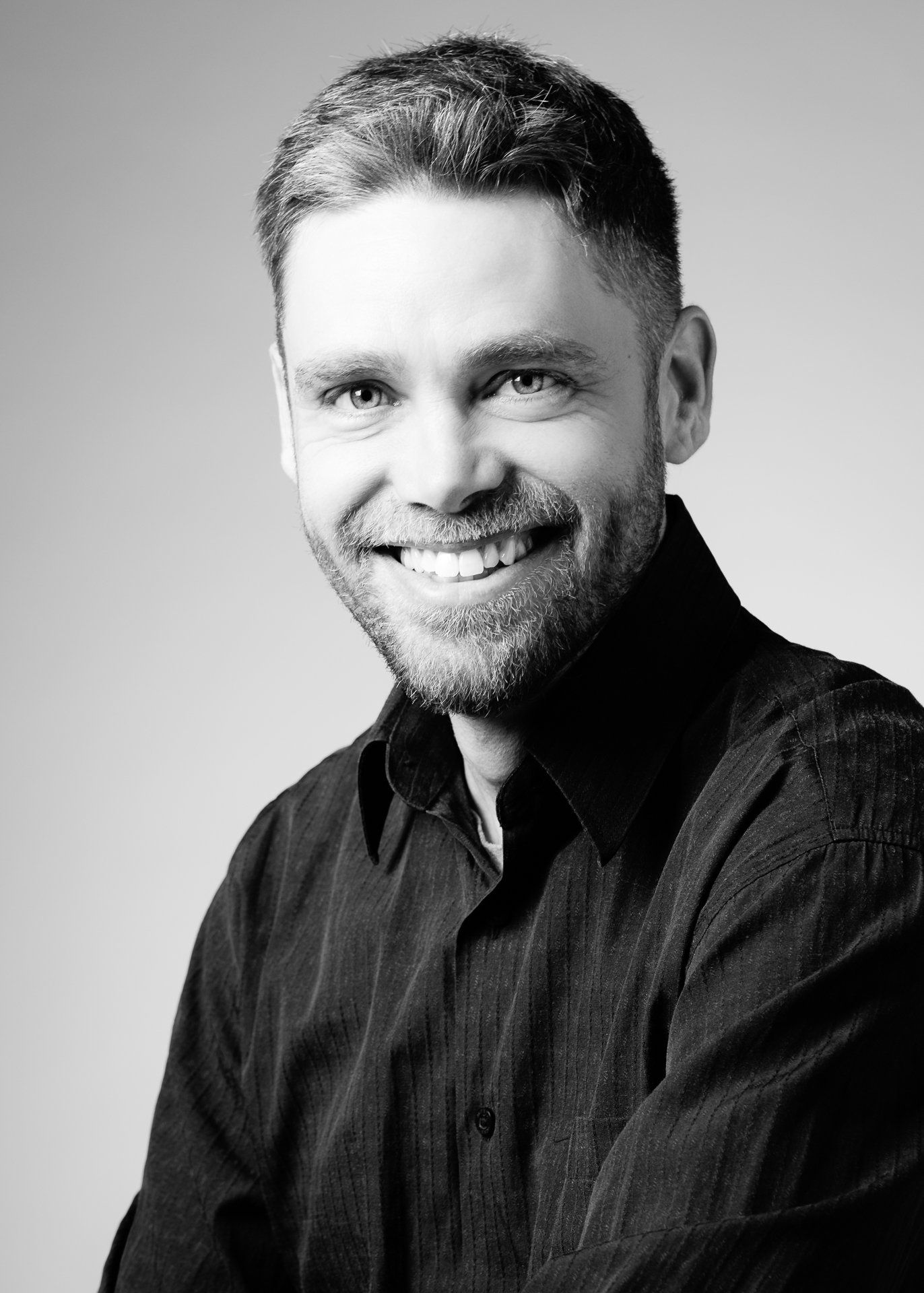 Homme aux cheveux courts, souriant, en chemise noire ; portrait.