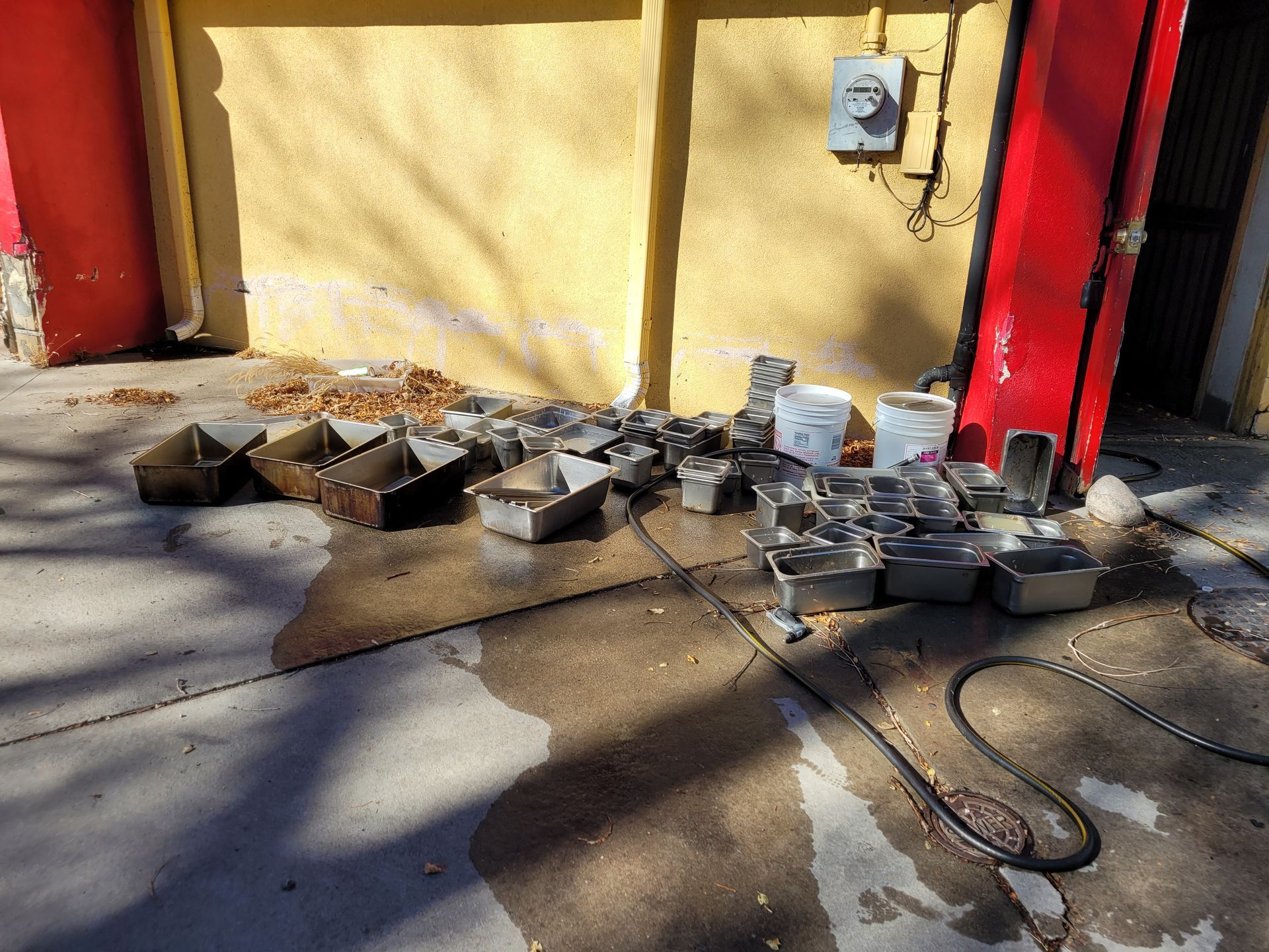 Scattered cinder blocks and debris on a sidewalk beside a yellow wall and red door in sunlight